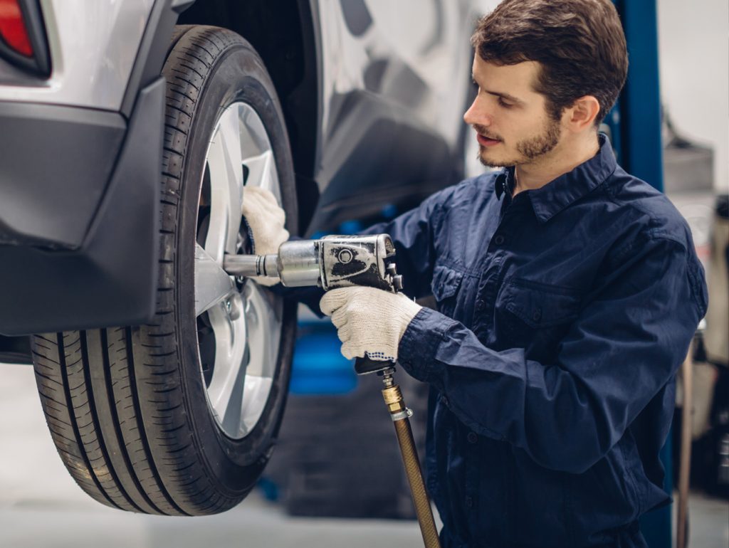 GMC Certified Technician with an electric tool is putting a tire on or off of an SUV