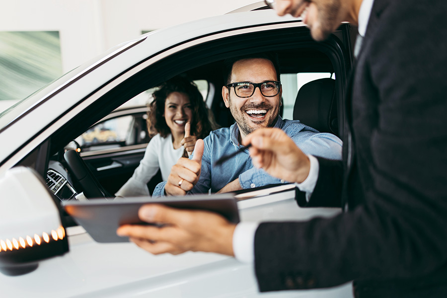 New Car Financing being shown to a couple in the GMC SUV in the showroom as they laugh enthusiastically, giving thumbs-ups signs to the smiling sales person