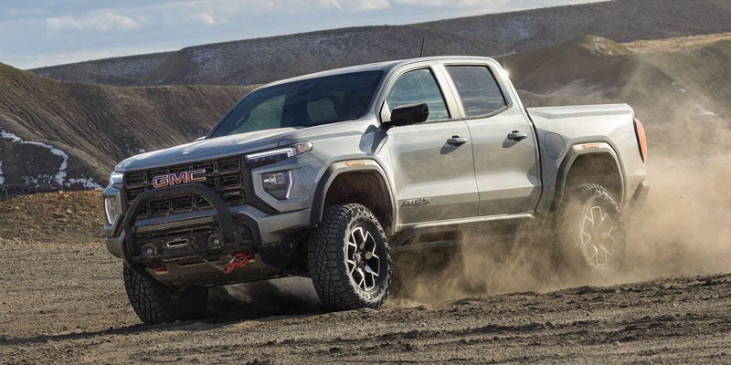 2026 GMC Canyon AT4 off-road pickup truck driving through dusty terrain